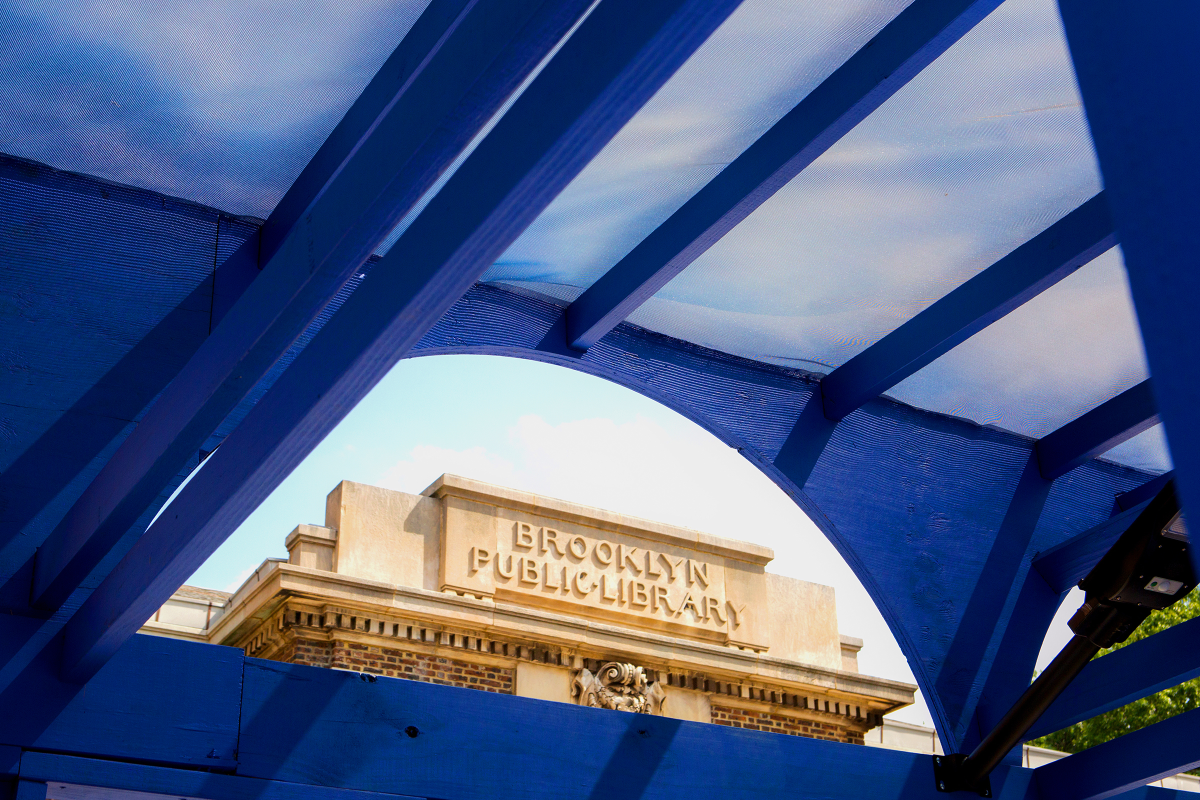 Close-up view of the Brooklyn Public Library sign framed by blue beams and a translucent awning.