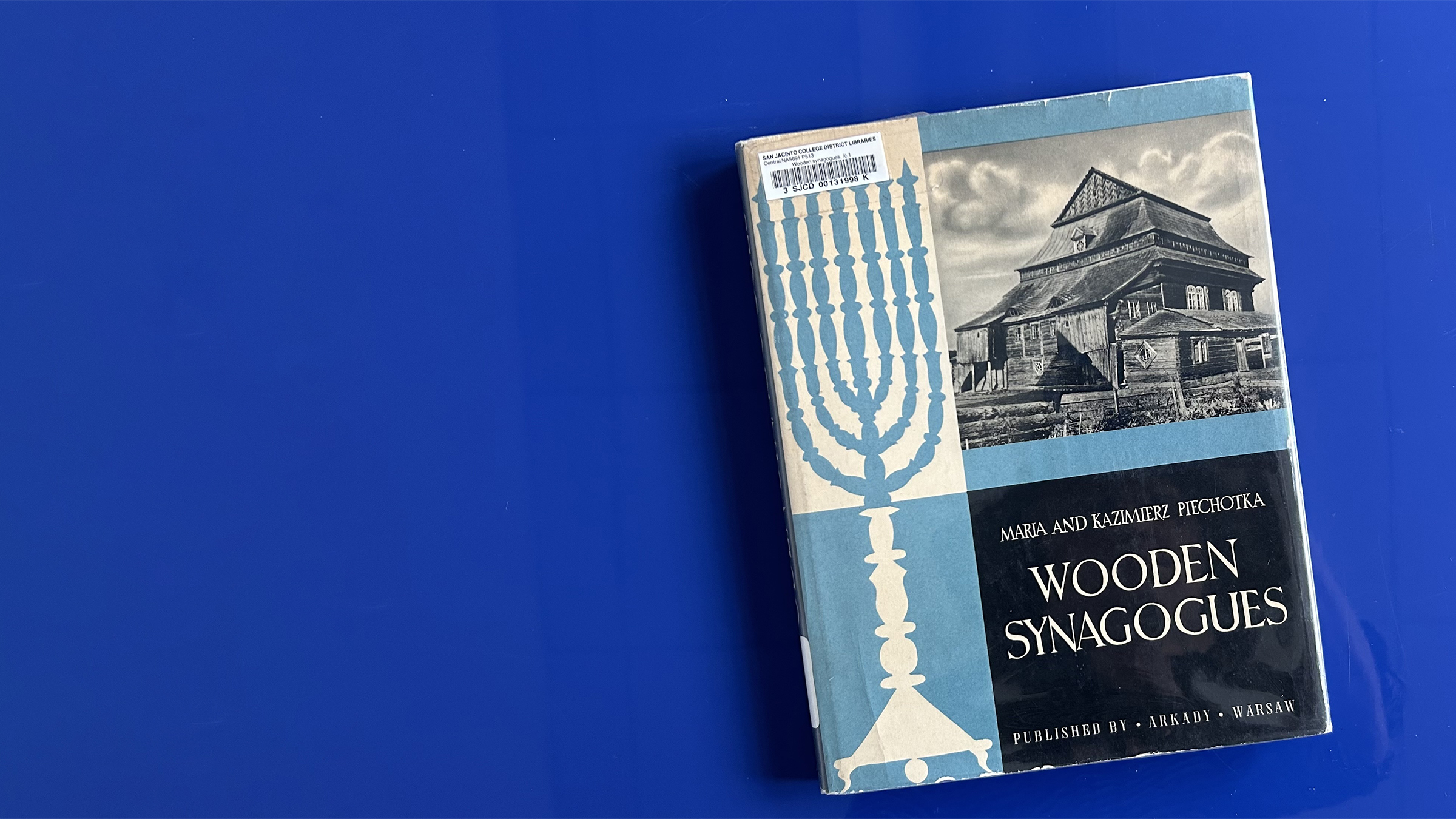 A book sitting on a blue table. The book is called "Wooden Synagogues" by Maria and Kazimierz Piechotka.