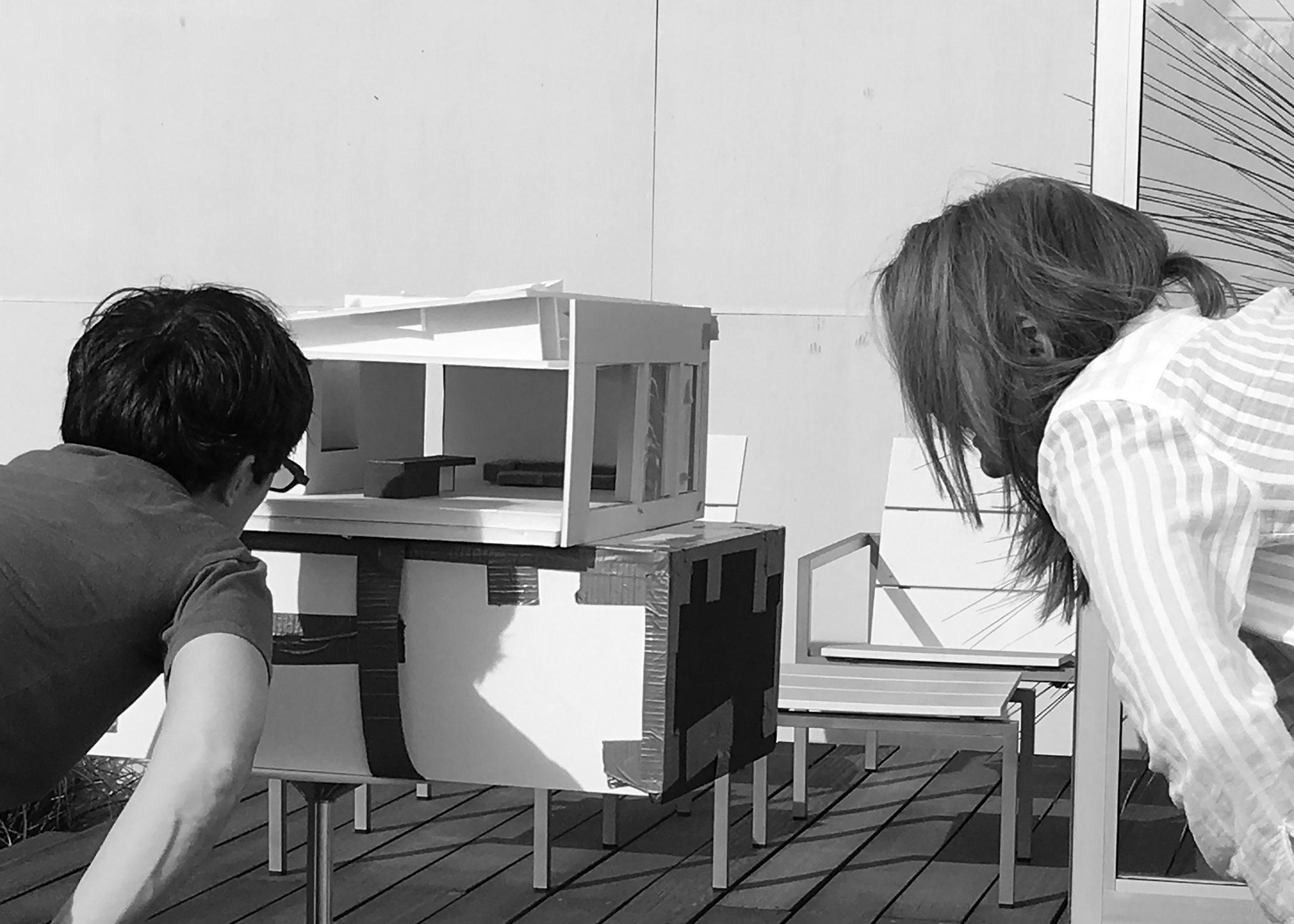 A black and white photo of the clients looking into a scale model of their home
