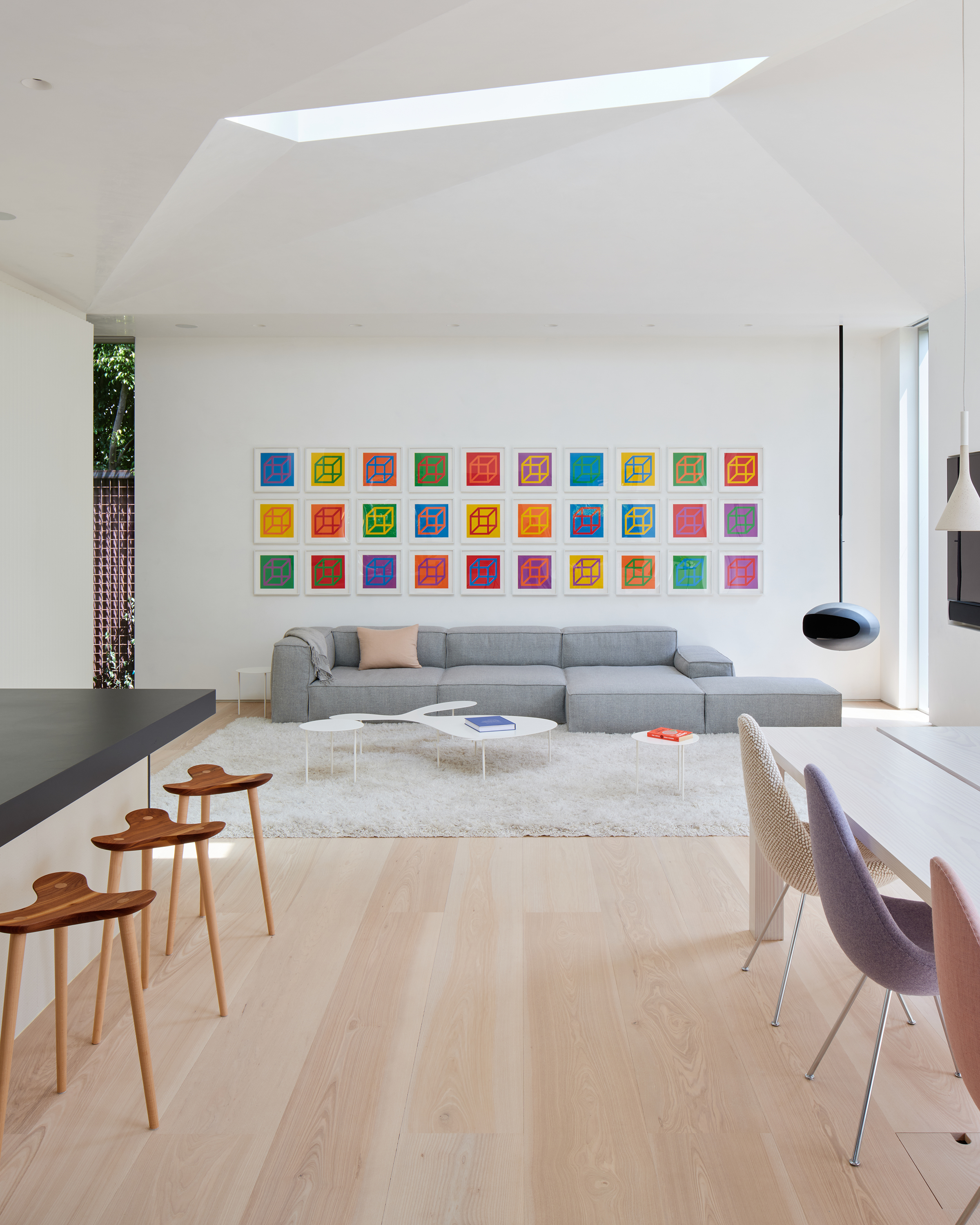 Elevational view of the furnished living area with a gird of artwork on the wall above the sofa and the faceted ceiling skylight above