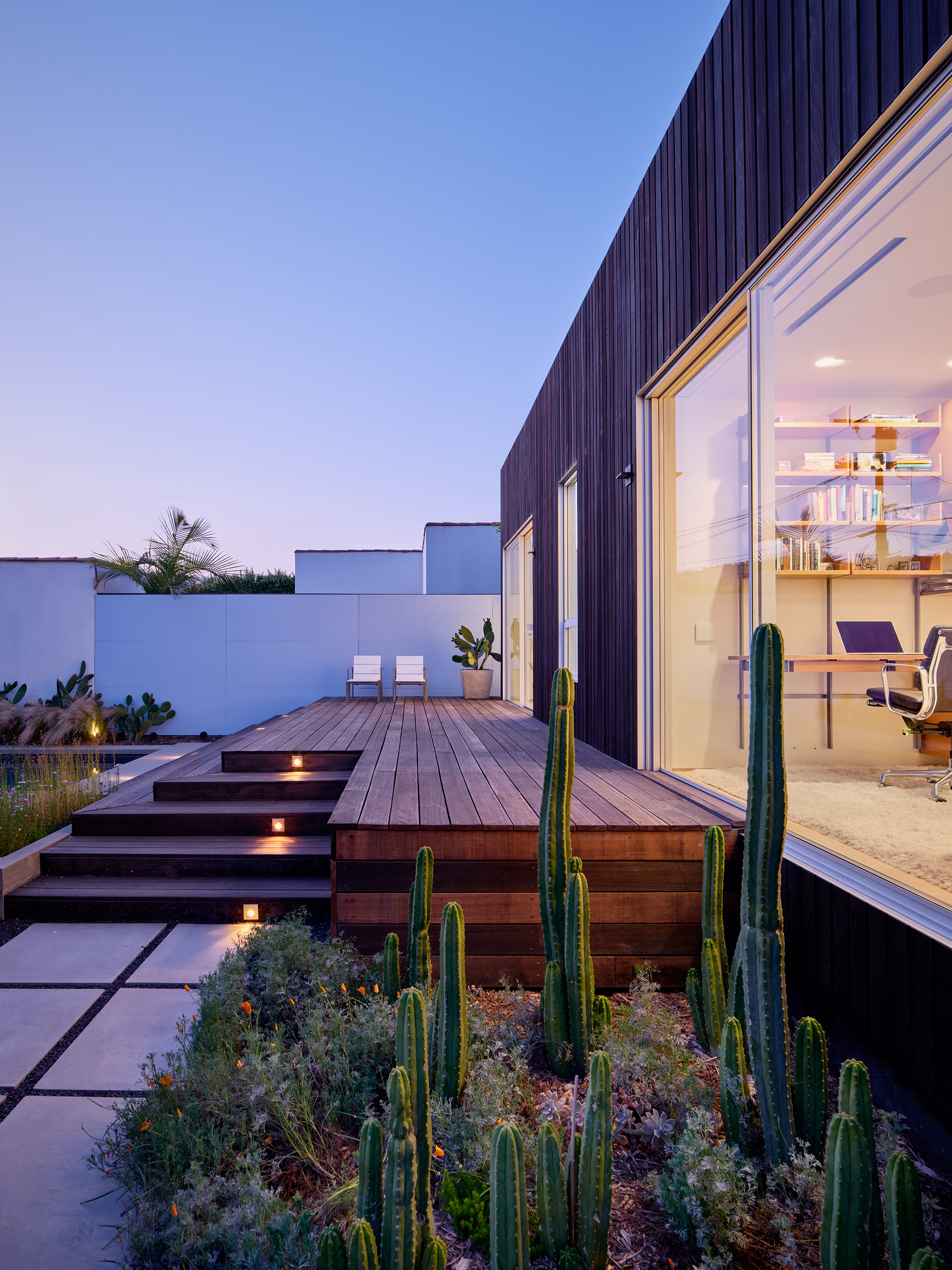Exterior view at sunset of the backyard deck and office space inside the full-height glass sliding doors.