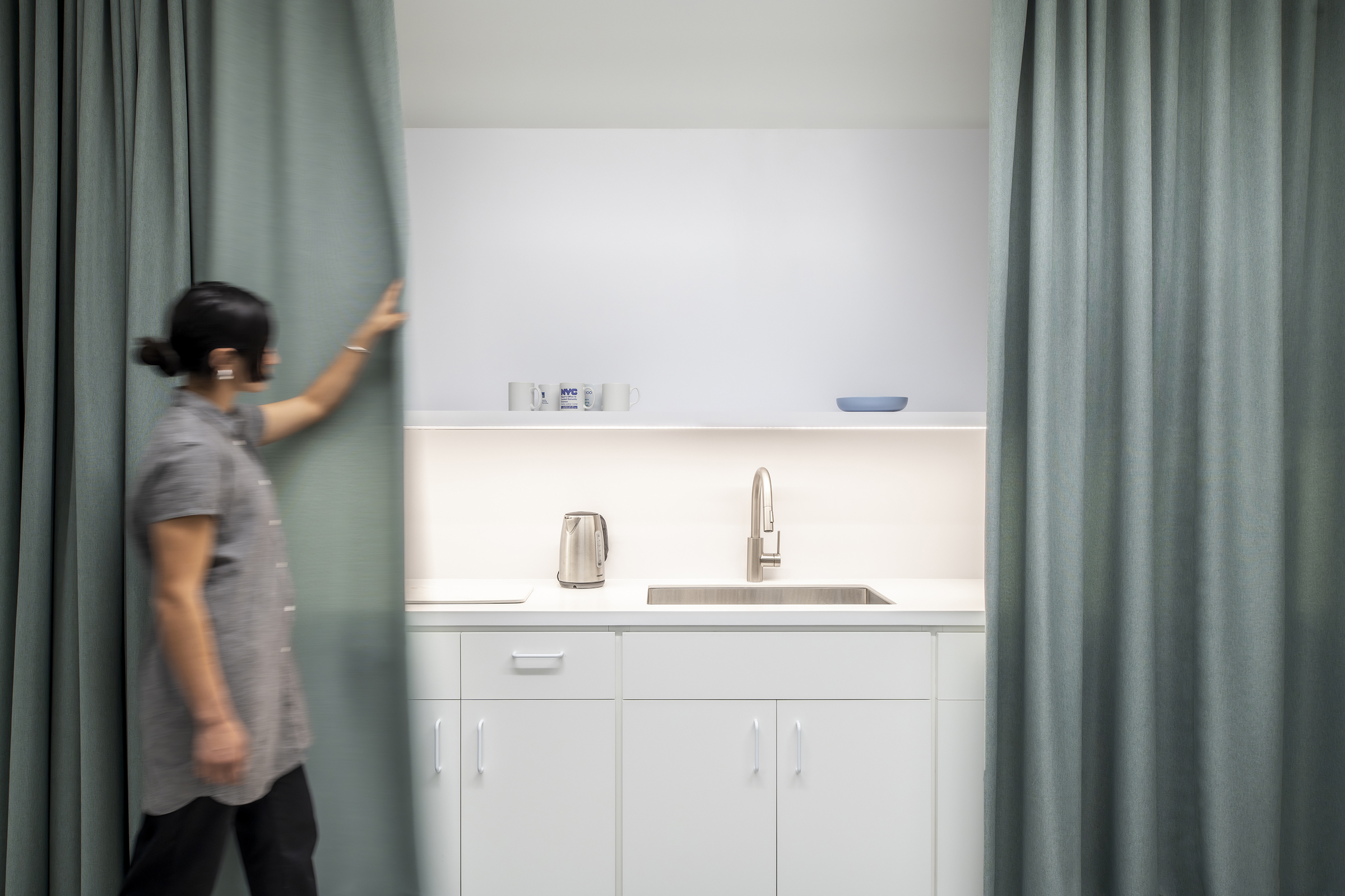 View of someone pulling curtains closed to conceal the kitchen sink and counter