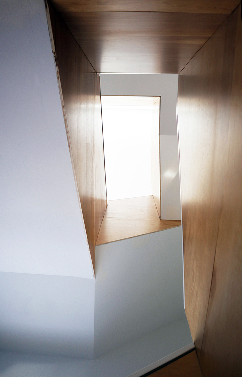 A view up the stair void, showing the warm wood paneling running up the height of the stair well. Natural light pours down from the top level and washes down the polished wood surfaces.