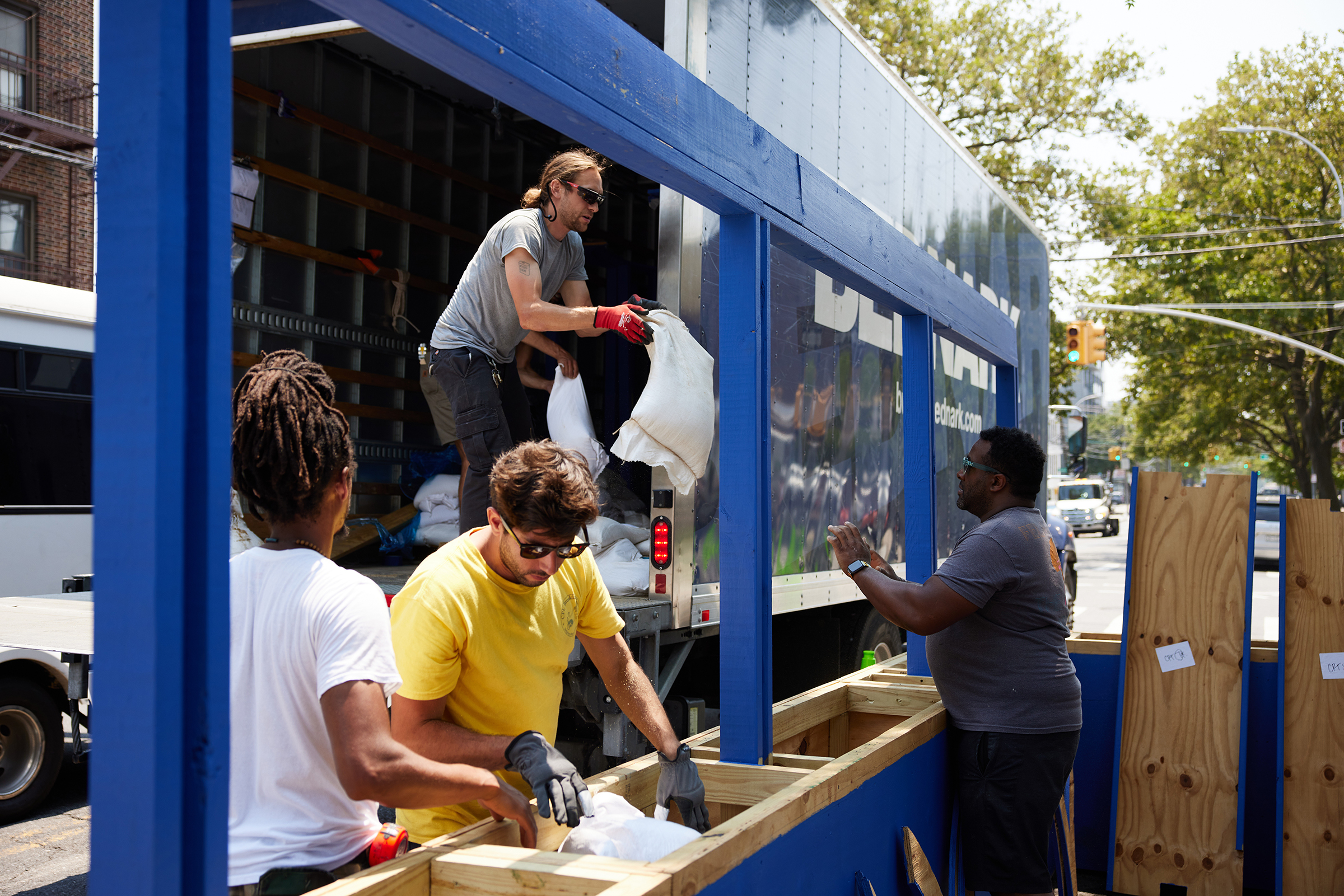 Four workers constructing a blue wooden structure outdoors on a sunny day.