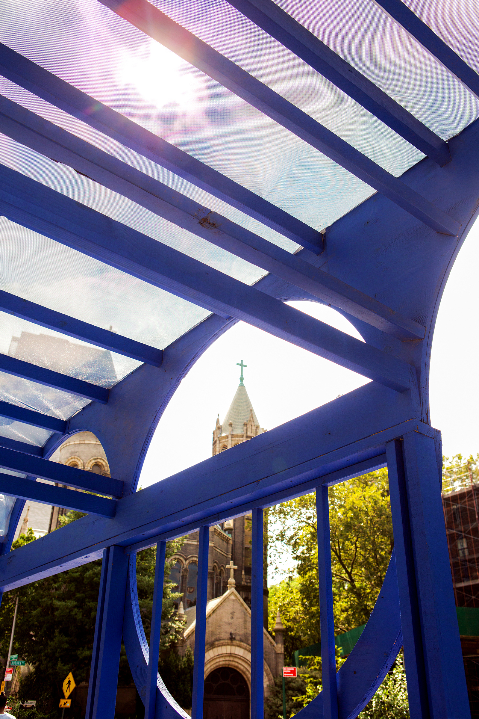 View of a church steeple through a blue arched wood structure with a translucent roof.